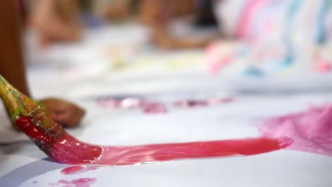 close up on paintbrush with wet red paint being brushed onto large white sheet of paper filmed in slow motion