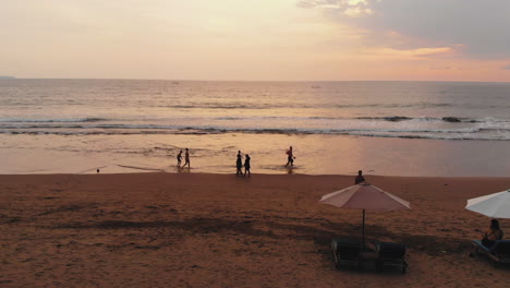 Luftaufnahmen-In-Zeitlupe-Von-Menschen,-Die-Während-Des-Sonnenuntergangs-Am-Strand-Spazieren-Gehen