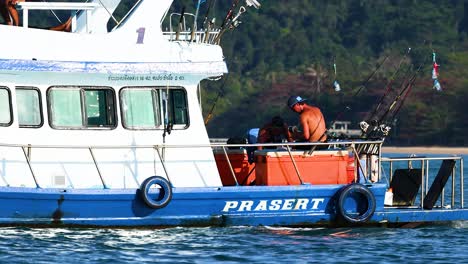 a fishing boat with crew engaged in activities on calm phuket waters. bright daylight enhances the vibrant scene