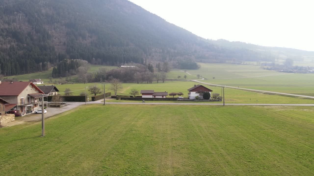 초록 잔디와 마을 집이 있는 으로 둘러싸인 개방된 도로에서 자전거를 타고 있는 자전거 타는 사람