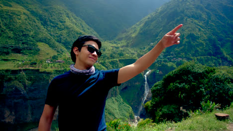 young man in sunglasses in green hilly landscape points finger to side