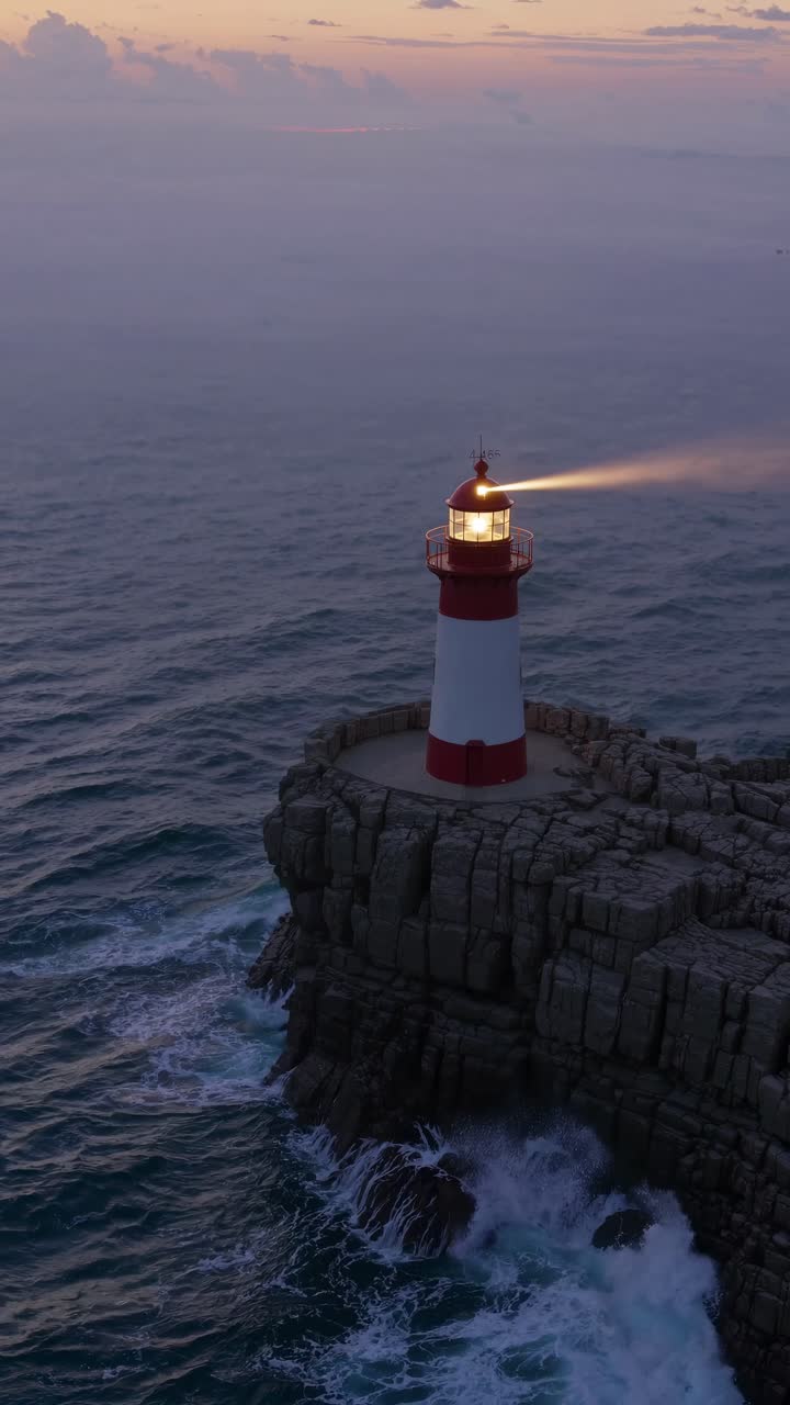 Vista aerea di un faro su una scogliera rocciosa al crepuscolo, con onde che si infrangono sotto