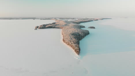 aerial, reverse, drone shot, of vuoniemi cape, in the middle of snowy lake saimaa, full of pine tree forest, at sunset, on a sunny, winter evening dusk, in north karelia, finland