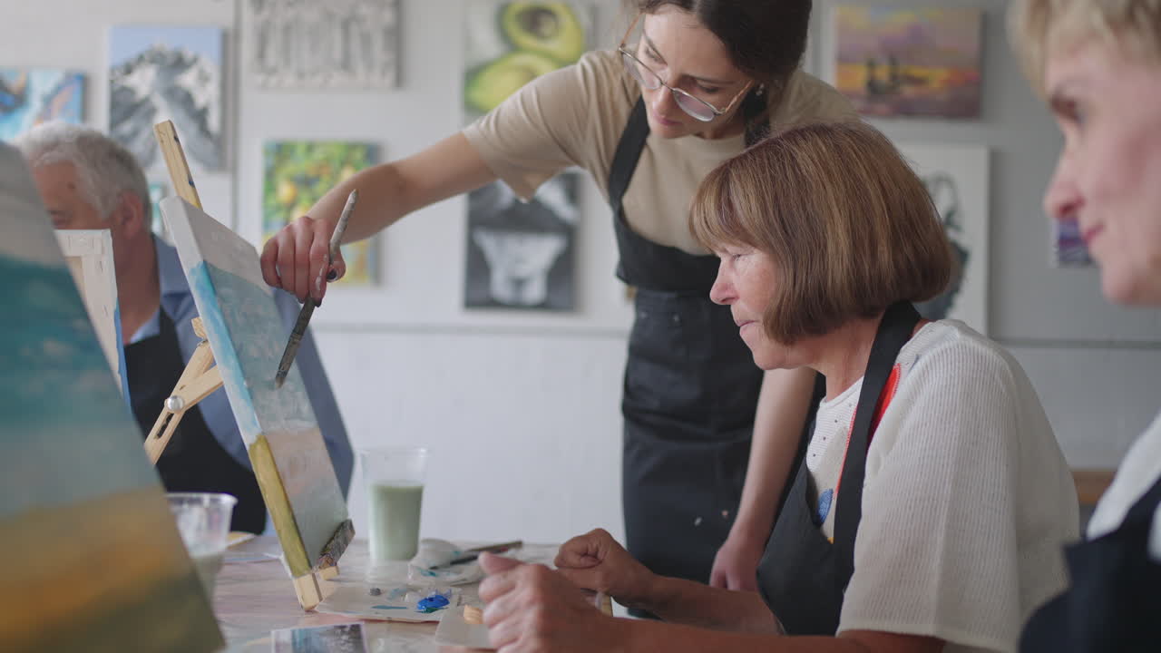 personas mayores en cámara lenta asisten a clases de dibujo. el maestro ayuda a los jubilados que asisten a clases de dibujo a dibujar. un grupo de amigos jubilados en una clase de dibujo