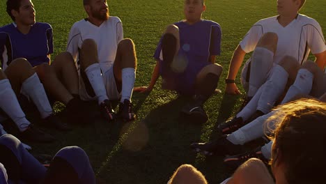 a soccer team sitting in a circle playing a fun game at sunset