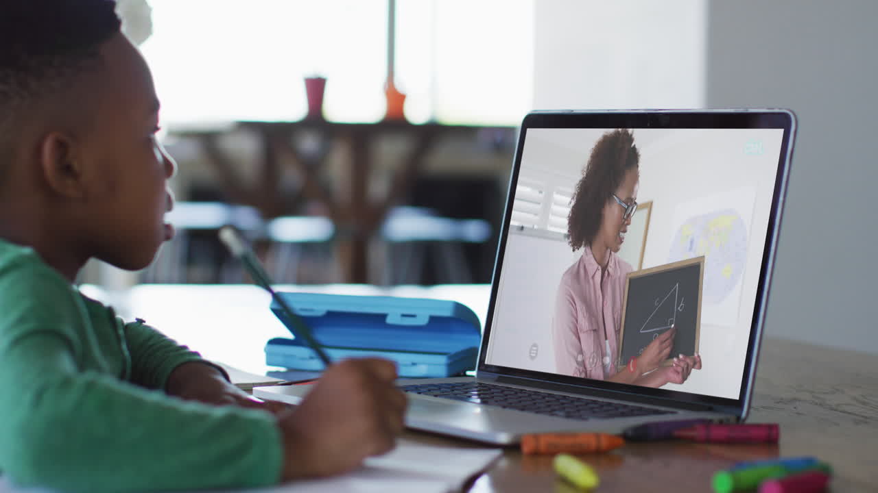 African american boy sitting at desk using laptop having online school lesson