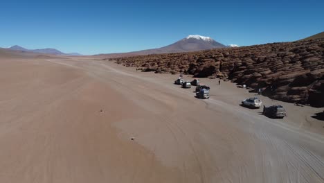 tourism trucks stop on bolivian altiplano desert by eroded rock bluff