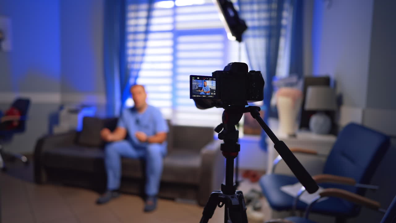 Footage of a video content in the office. Male doctor in blue uniform taking video on the modern camera. Selective focus