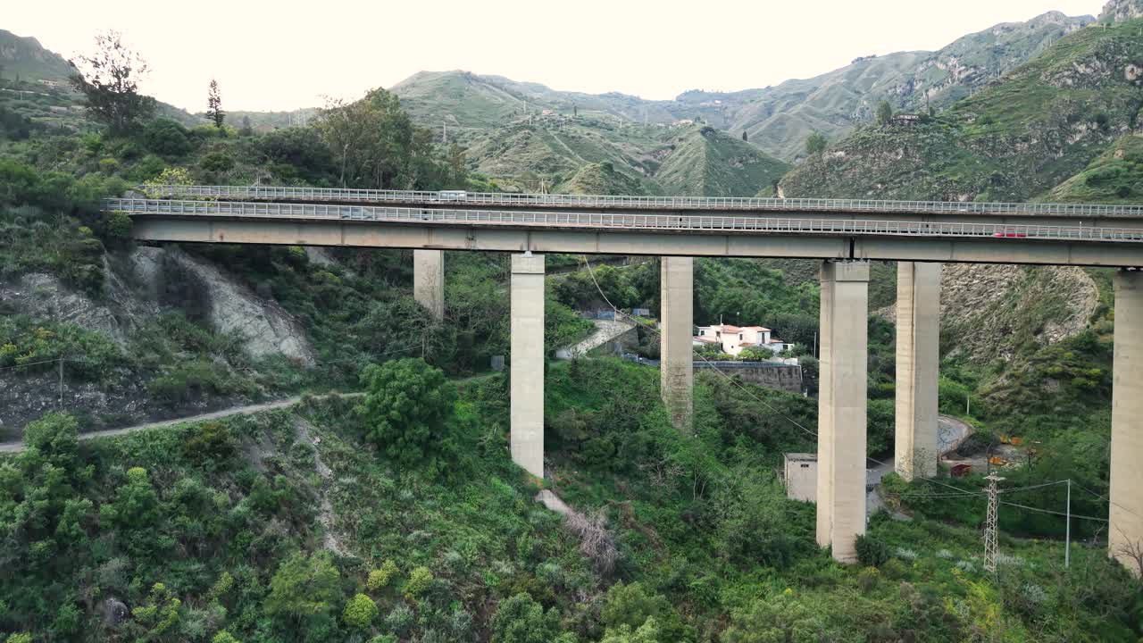 Aerial tilt up parallax of elevated bridge stretching across rolling hillsides near Taormina mountains
