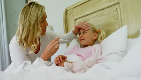 Mother-checking-sick-daughter-temperature-with-digital-thermometer-in-the-bedroom-4k