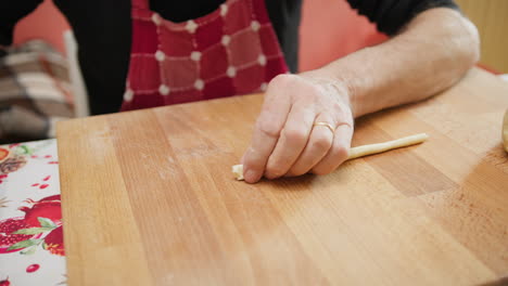 mans hands rolling and splitting raw dough for italian pasta