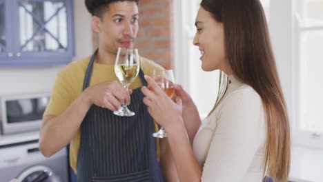 feliz pareja biracial cocinando juntos y bebiendo vino en la cocina