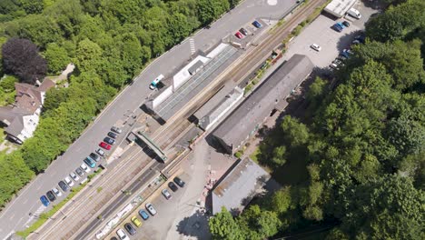 Aerial-orbital-view-of-Okehampton-Station-surrounded-by-greenery-in-Devon,-UK