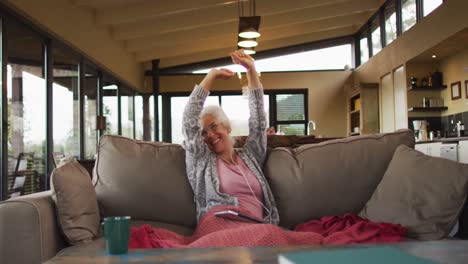 senior mixed race woman sitting on sofa celebrating