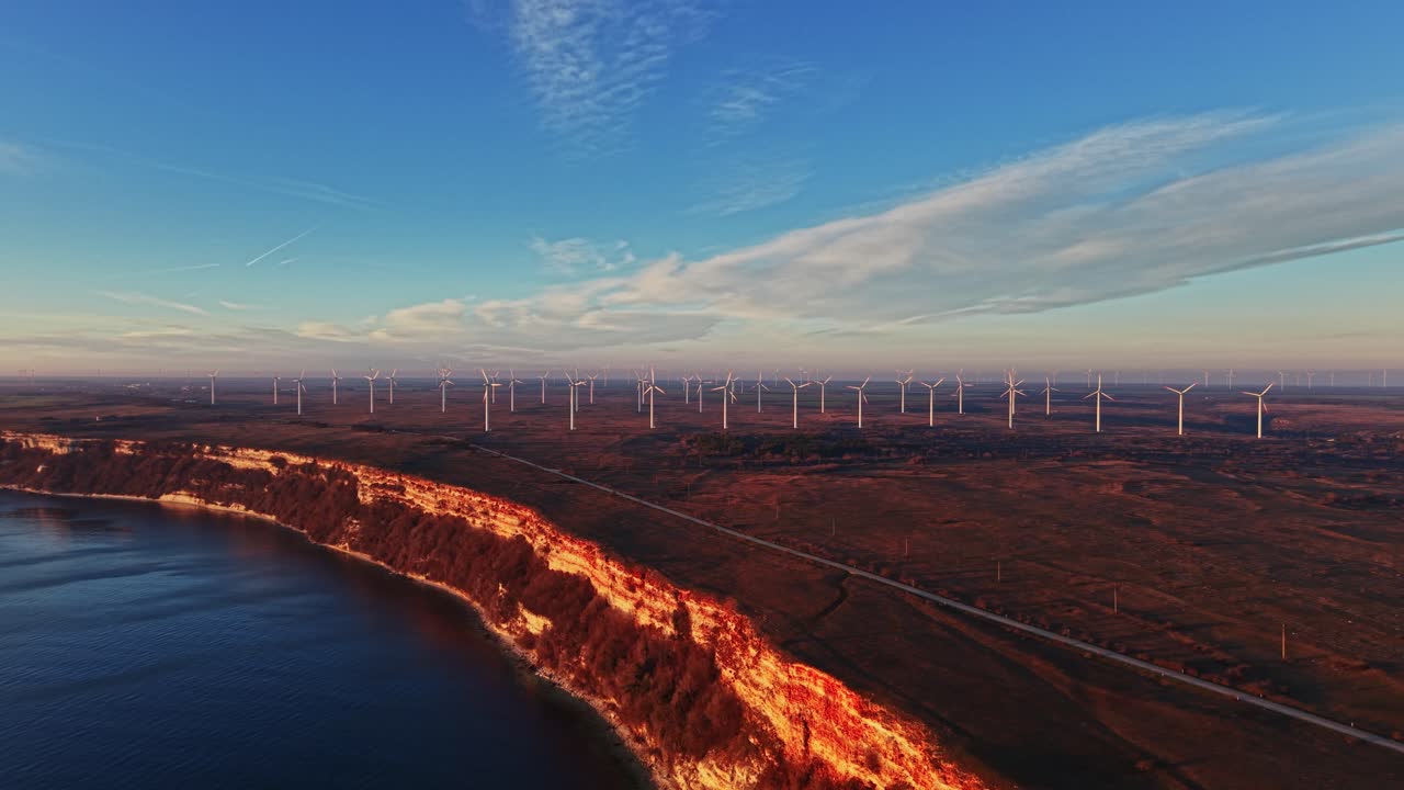 Turbinas eólicas ao longo da costa ao pôr do sol perto de um penhasco rochoso