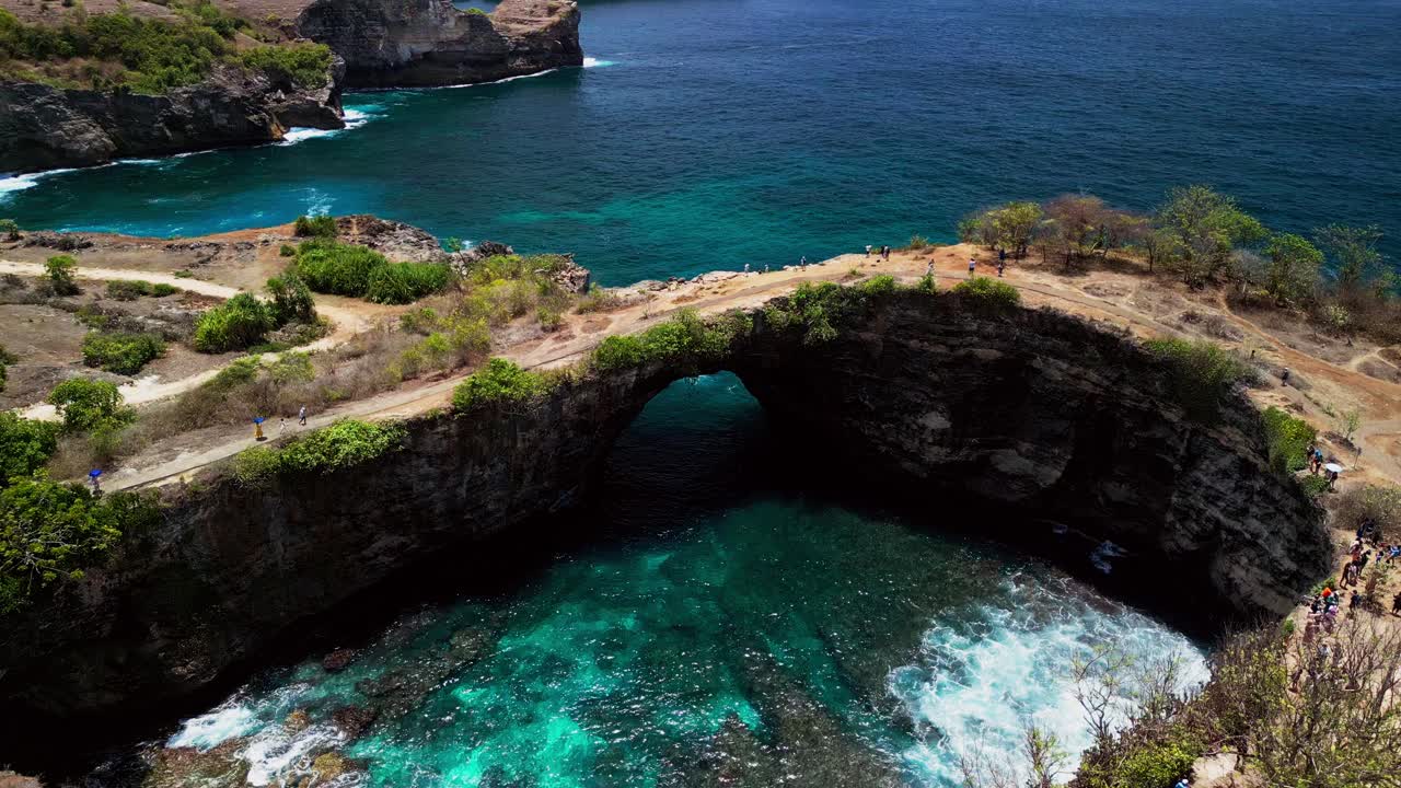Aerial views of Broken Beach on Nusa Penida reveal a breathtaking natural bridge and clear waters below surrounded by cliffs where nature and ocean forces have shaped the dramatic landscape.