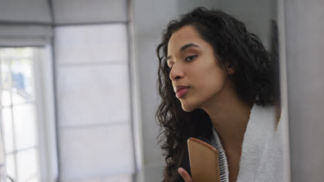 Mixed-race-woman-brushing-her-hair-in-bathroom