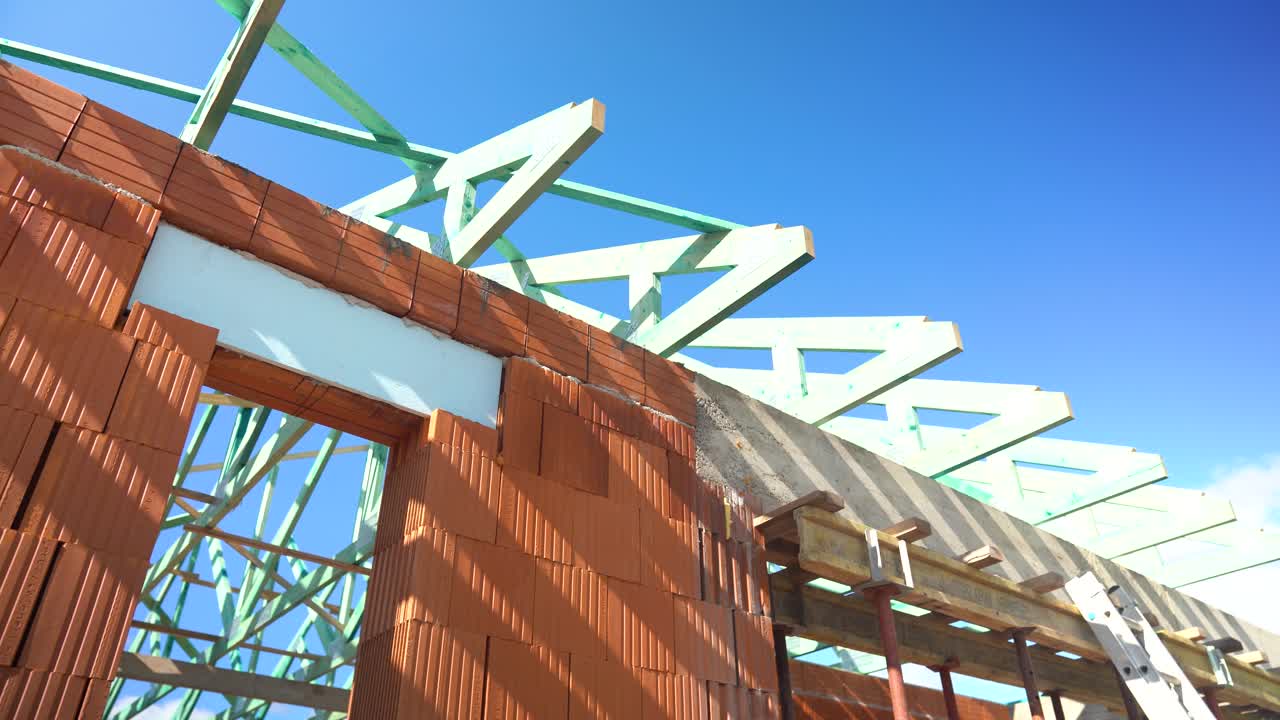 Timber roof truss installation over brick structure during construction on bright sunny day