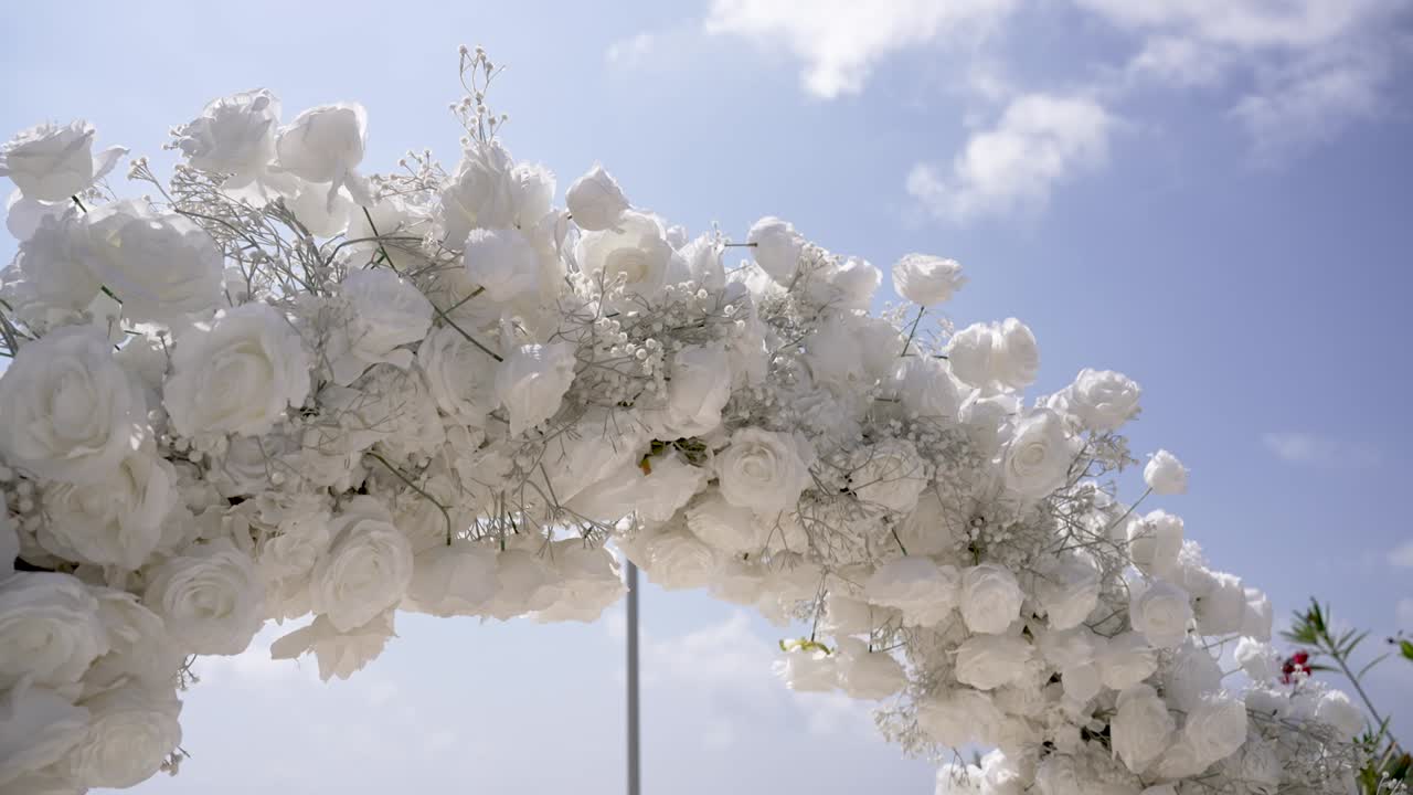 Stunning white flower arch enhances the beauty of the outdoor setting. Perfect for a wedding or special gathering, showcasing a bright blue sky filled with light
