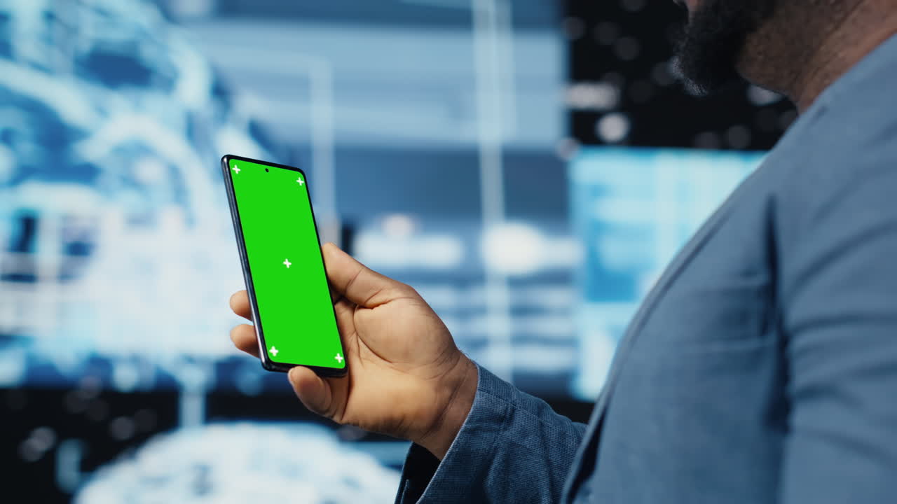 Focused black IT professional looks at phone with green screen