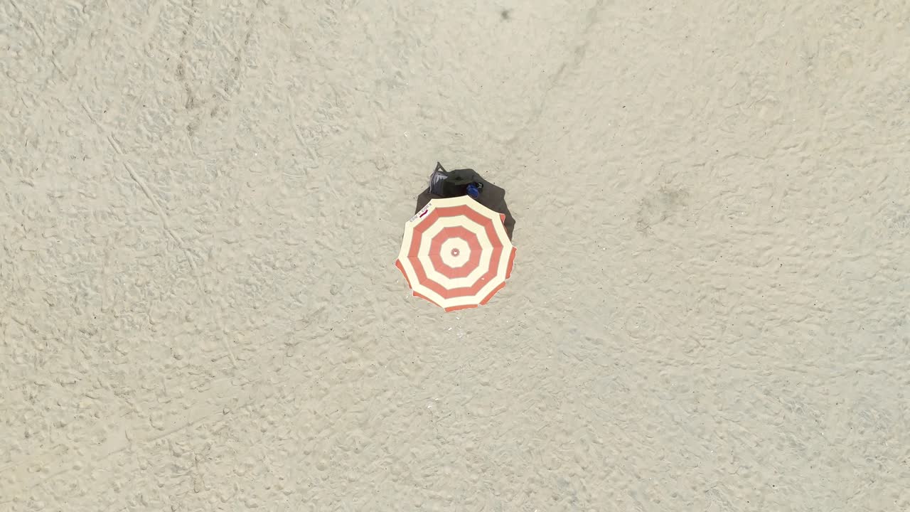 Top-down drone view of a single beach umbrella on the golden sand of Banjul, Gambia, symbolizing relaxation and tourism