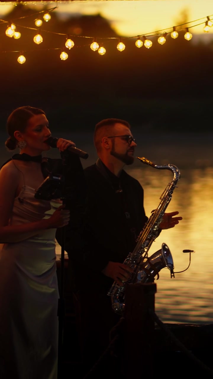 Duo musicale che si esibisce dal vivo al tramonto con luci a catena