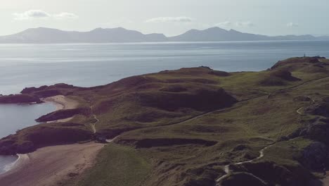 Aerial-view-across-idyllic-Ynys-Llanddwyn-island-with-hazy-Snowdonia-mountain-range-parallax-across-shimmering-Irish-sea-at-sunrise