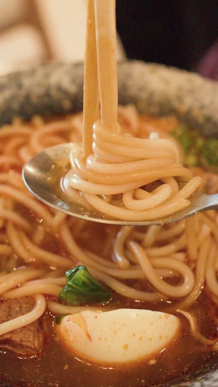Primo piano di noodles Mee Shay birmani sollevati con bacchette e un cucchiaio a Bangkok.