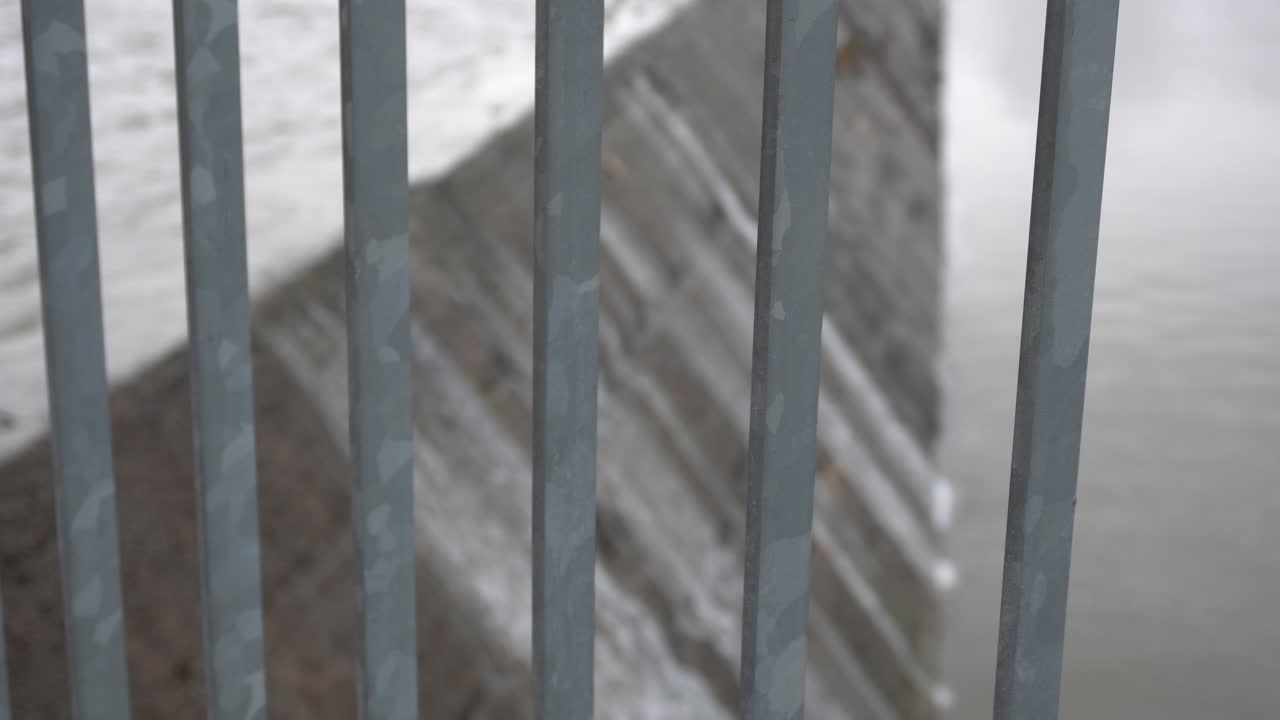 From the angle, you can see a fence on a cloudy day. Behind, you have a dam and the water in a continual loop pattern.