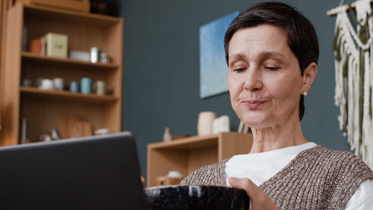 Mature woman eating a meal while using a laptop at home