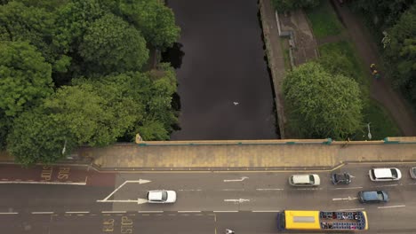 A-smooth-drone-shot-across-a-busy-road,-over-a-city-river-|-The-Water-of-Leith,-Edinburgh,-Scotland-|-Shot-in-4k-at-30-fps