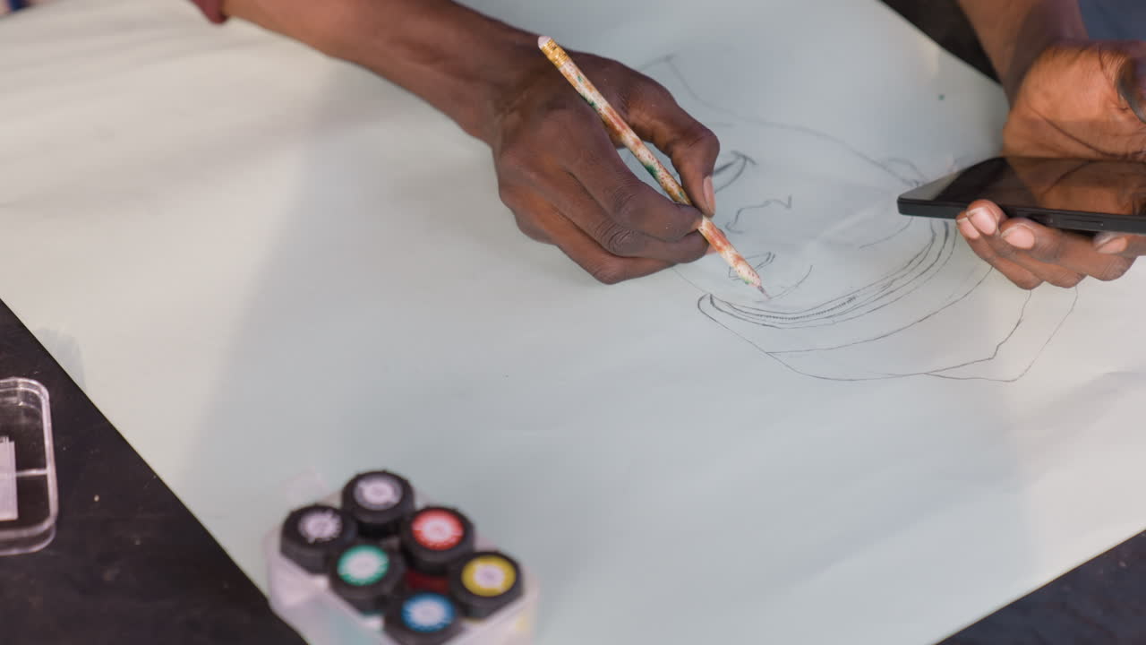 Black artist sketching portrait on paper using gouache palette and pencil, creating dotted guide lines while referencing phone for pose. Closeup hands show deliberate strokes, textured paper, patient
