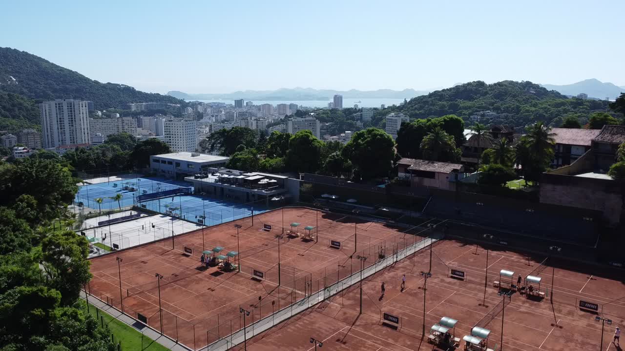 Canchas de tenis al frente y edificios y mar al fondo.