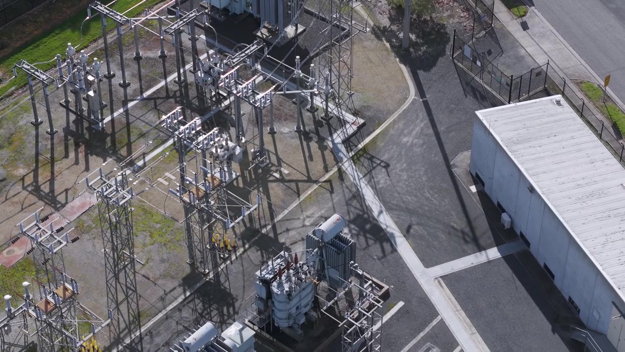 Drohnenaufnahme, die sich langsam über ein Elektrizitätswerk und Hochspannungsleitungsmasten bewegt.