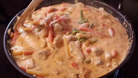 creamy curried chicken, vegetables meal stirred in hot pan with fork