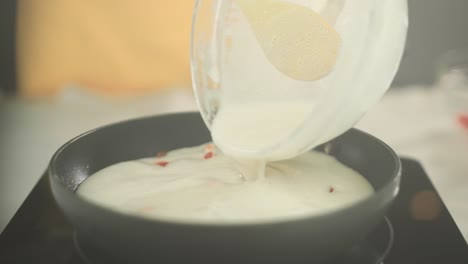 primer plano de cocinar rodajas de tomate en una sartén con salsa bechamel vegana que se agrega y se coloca una tapa en la sartén