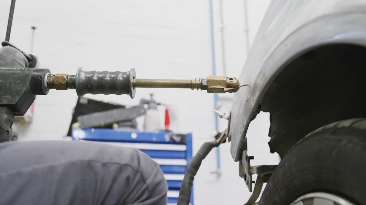 mecánico de automóviles afroamericano que sostiene un destornillador y usa un martillo para reparar un automóvil