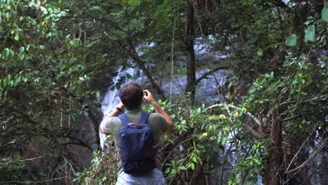 young travel man walking on waterfall and take photos and videos on phone