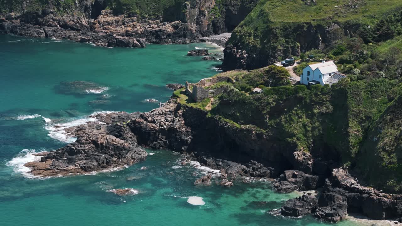 Flyover of cliffside ruins on the Cornwall coast with turquoise sea and sunlit green hills in the background