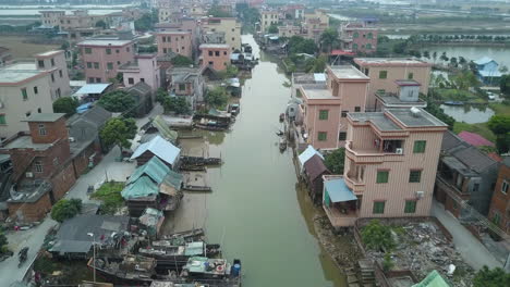 Toma-Aérea-De-Un-Pueblo-Asiático-Ubicado-A-Lo-Largo-De-Un-Río-Contaminado-Con-Botes-Amarrados