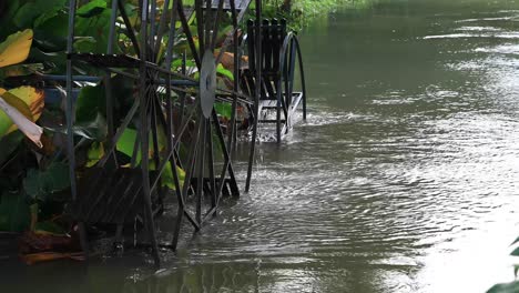 4k waterwheel spinning slowly with wooden paddles and metal frame in a flowing river