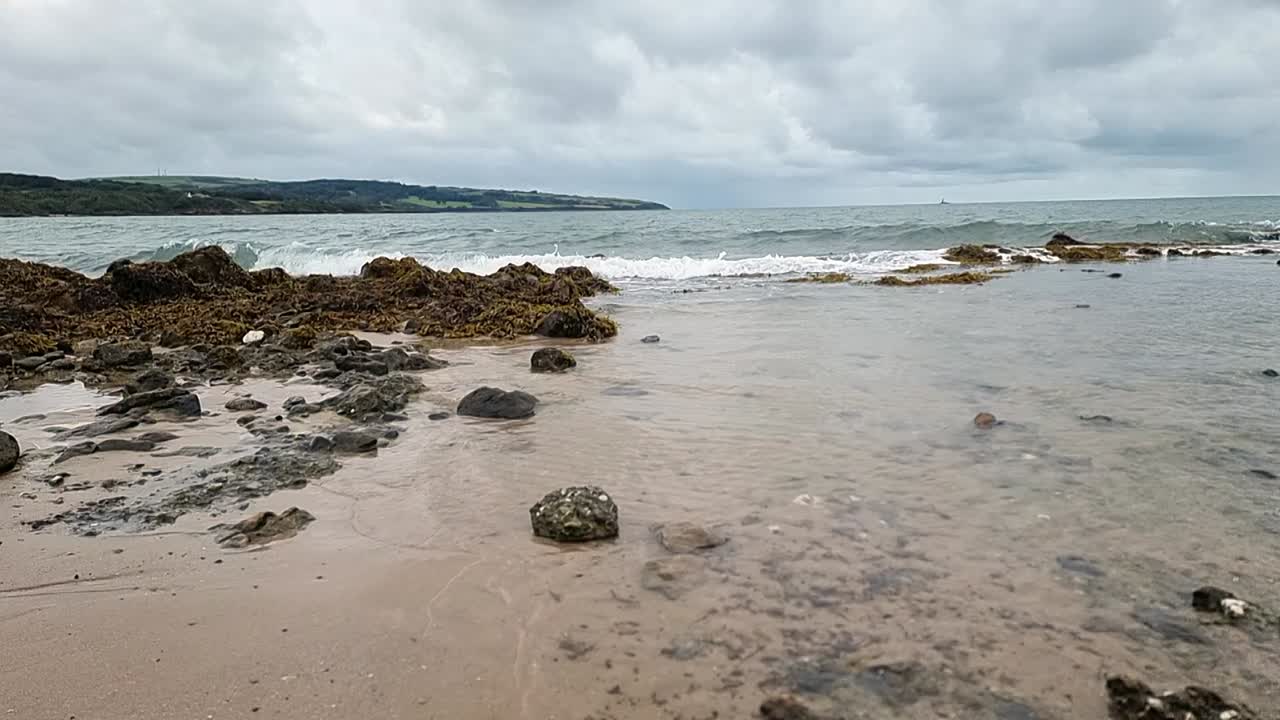 Slow motion sea waves leaving transparent clear water over sandy Anglesey beach coastline