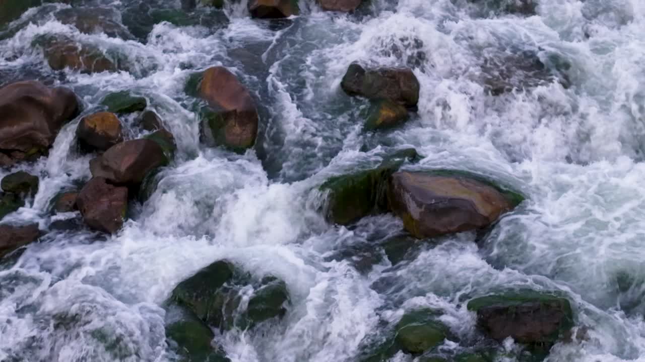 Una piccola cascata si riversa da una bassa sporgenza rocciosa in un fiume, creando acqua bianca spumeggiante e correnti vorticose.