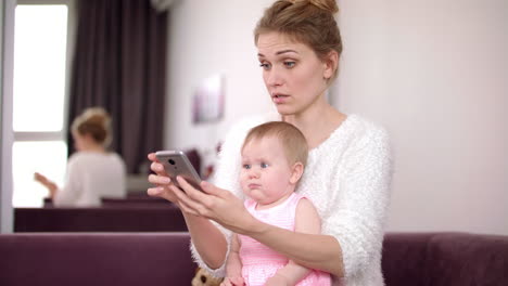 Frau-Mit-Baby-Hält-Telefon-Zu-Hause