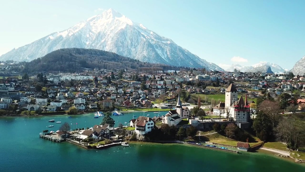 Toma de alejamiento con dron de la ciudad de Spiez, su castillo e iglesia en el lago Thun con el monte Niesen cubierto de nieve al fondo, mostrando la belleza del Oberland bernés, Suiza.