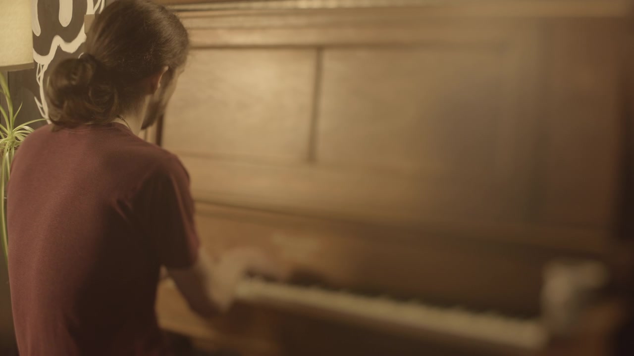 Selective focus on pianist practicing from behind in indoor setting, tilt lens