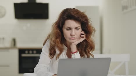 serious woman reading news on laptop at open kitchen. young lady drinking tea