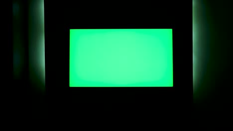 tv with horizontal green screen on a black wall with green illumination. concept. close up of chroma key tv screen in a dark room at night