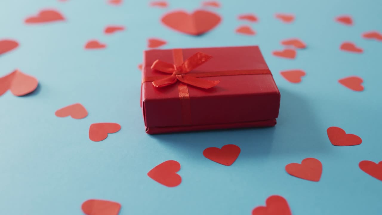 Multiple red paper hearts and red present at valentine's day on blue background
