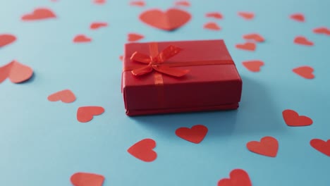 Multiple-red-paper-hearts-and-red-present-at-valentine's-day-on-blue-background